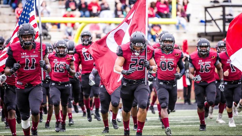 Football team runs onto the field at start of game carrying flags